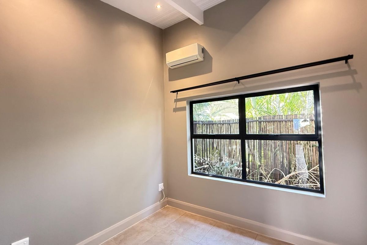 A bright, empty bedroom featuring tiled flooring, a modern black-framed window, and a wall-mounted air conditioning unit.