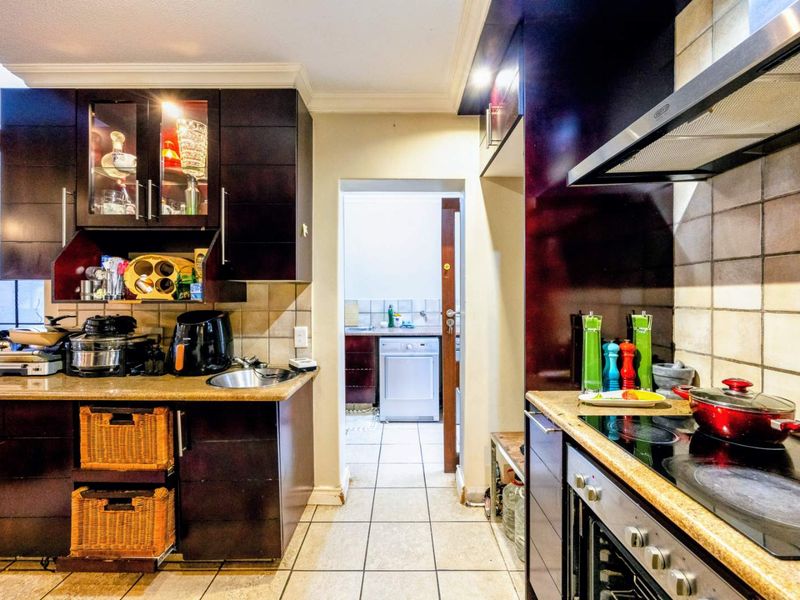 A functional kitchen featuring dark wood cabinetry, granite countertops, built-in oven, and hob, with an adjacent scullery area visible through the doorway.
