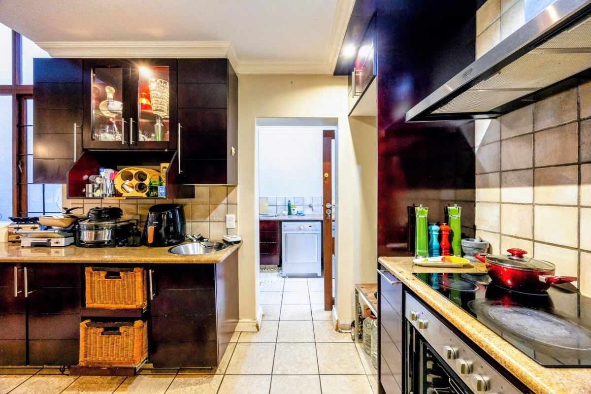 A functional kitchen featuring dark wood cabinetry, granite countertops, built-in oven, and hob, with an adjacent scullery area visible through the doorway.