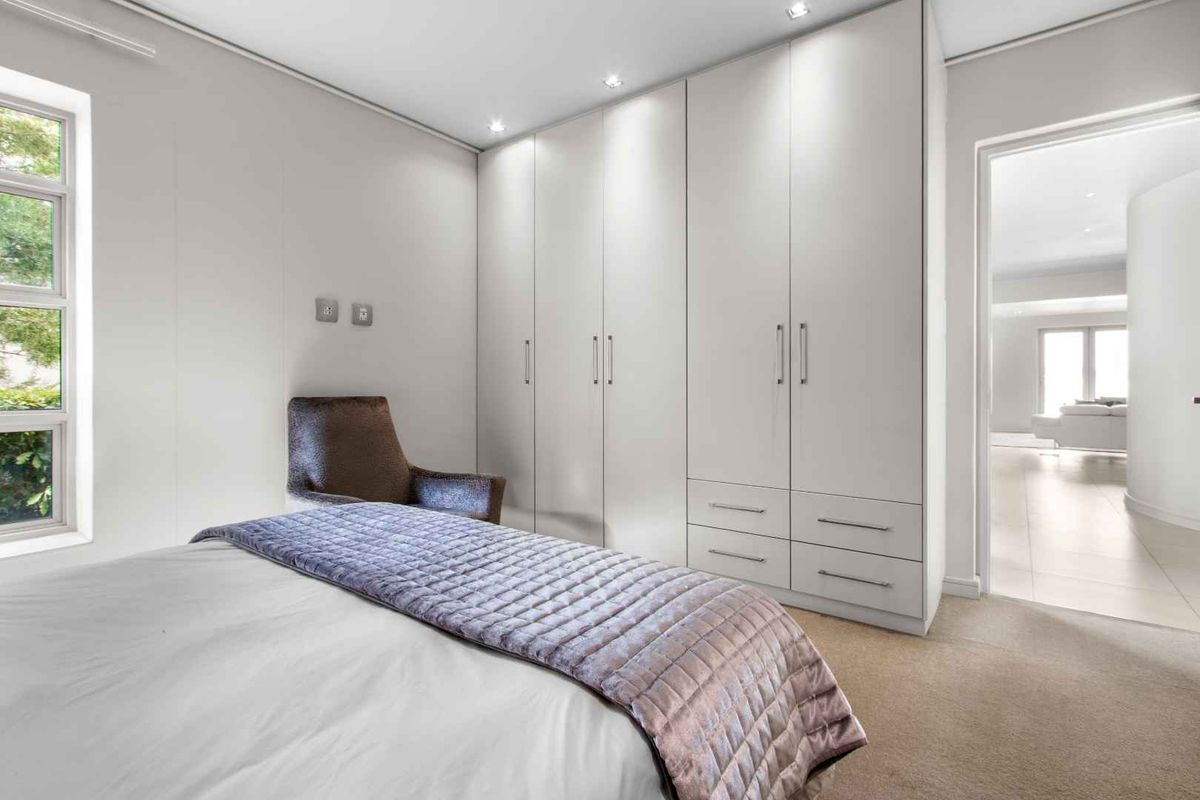 A bright and modern bedroom featuring extensive floor-to-ceiling built-in cabinetry, recessed downlighting, and large windows allowing for ample natural light.