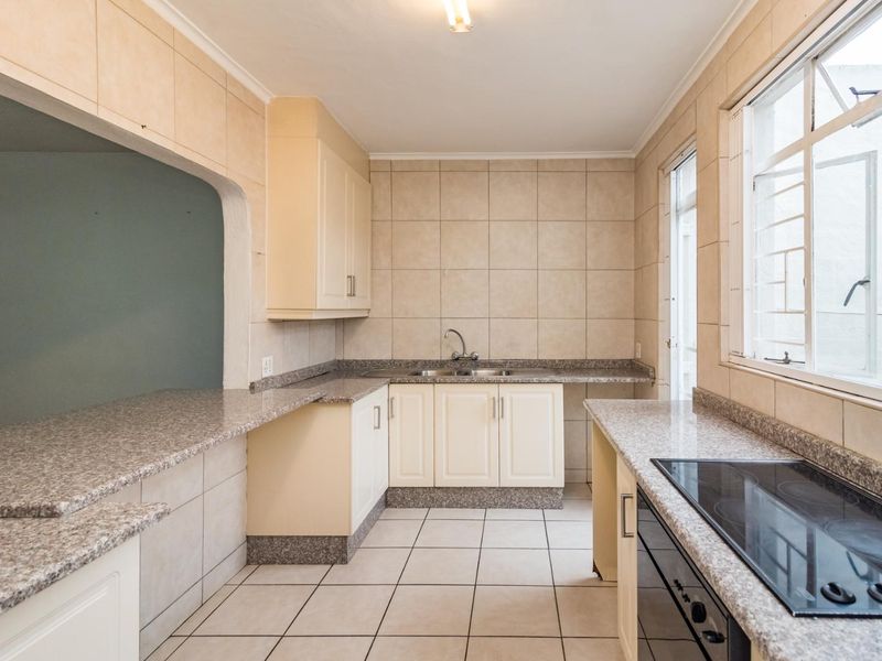 Functional kitchen featuring granite countertops, built-in cabinetry, electric hob, oven, and ceramic tile finishes throughout.