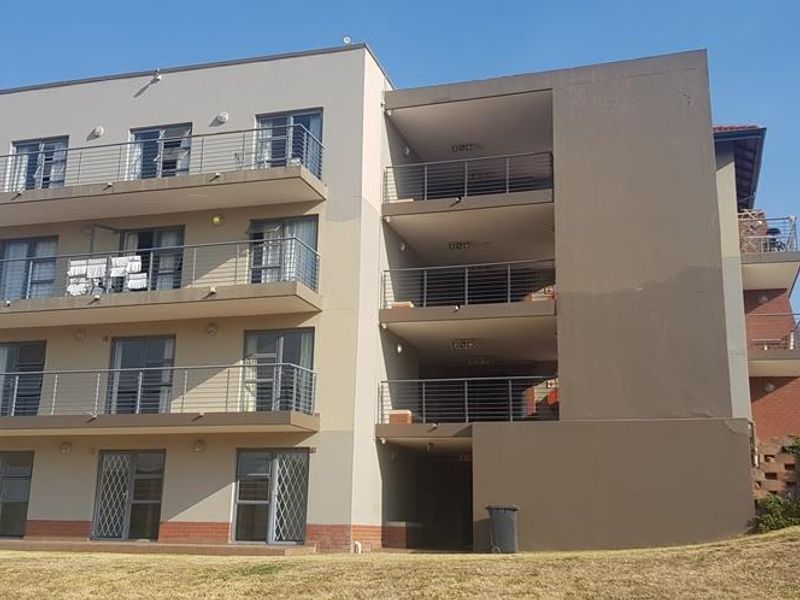 Rear elevation of a multi-story apartment building featuring stacked balconies with metal railings and sliding glass door access.