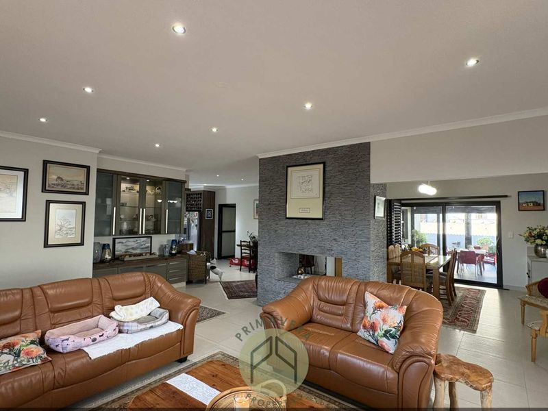 Spacious open-plan living area featuring a central stone-clad fireplace, recessed lighting, built-in cabinetry, and seamless access to the outdoor patio through sliding glass doors.