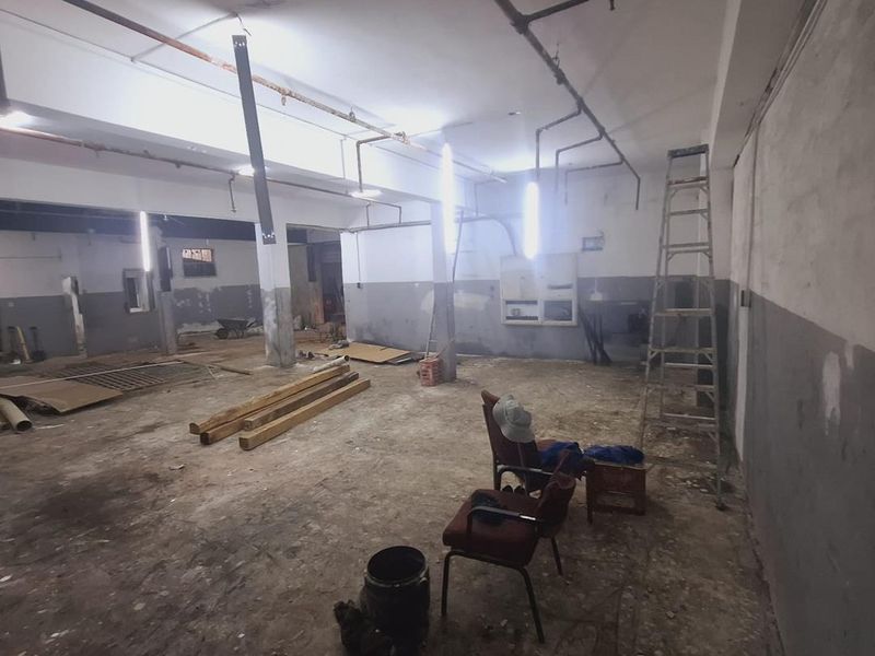 An industrial utility space featuring exposed ceiling pipes, concrete flooring, and support columns, currently in a shell condition suitable for renovation.