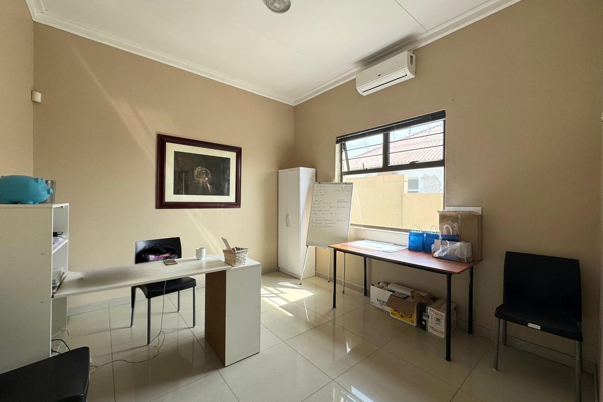 A functional office space featuring tiled flooring, a wall-mounted air conditioning unit, and natural light from a window.
