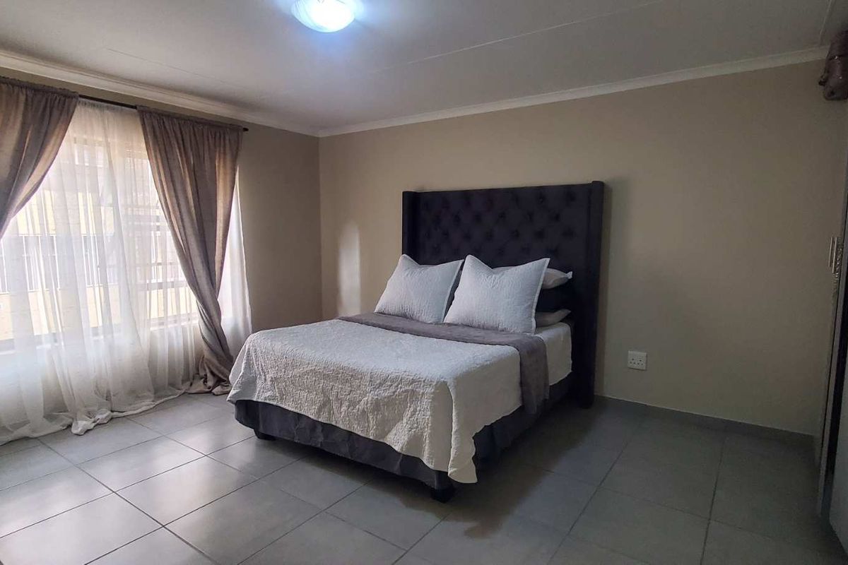 A spacious bedroom featuring neutral wall tones, tiled flooring, and a built-in wardrobe, offering a clean and functional living space.