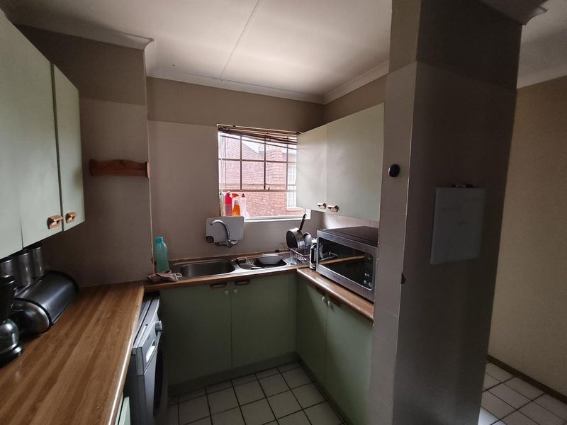 A compact kitchen featuring laminate countertops, built-in cabinetry, and a stainless steel sink, offering a functional layout with potential for modern updates.