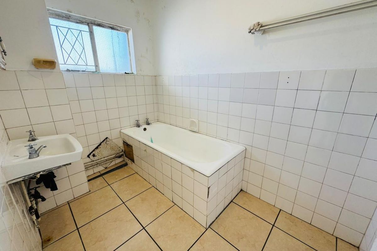A dated bathroom featuring a bathtub, wall-mounted basin, and tiled finishes, currently requiring significant maintenance and cosmetic renovation.