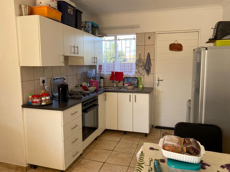 Functional kitchen featuring white cabinetry, laminate countertops, built-in oven and hob, tiled backsplash, and direct access to the exterior.