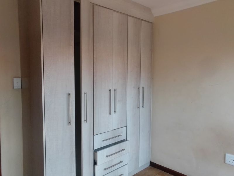 A bedroom featuring light wood-finish built-in cupboards with integrated drawers and tiled flooring.