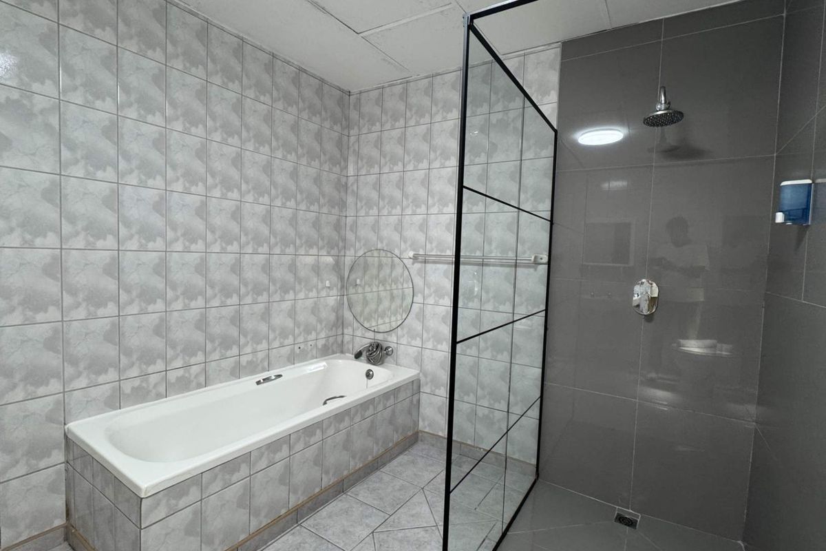 Modern bathroom featuring a built-in bathtub, a separate walk-in shower with a black-framed glass screen, and contemporary grey wall and floor tiling.