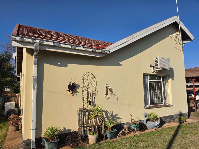 Rear exterior view of the house featuring a tiled roof, wall-mounted air conditioning unit, and security-barred windows with visible maintenance required on fascia and plaster.