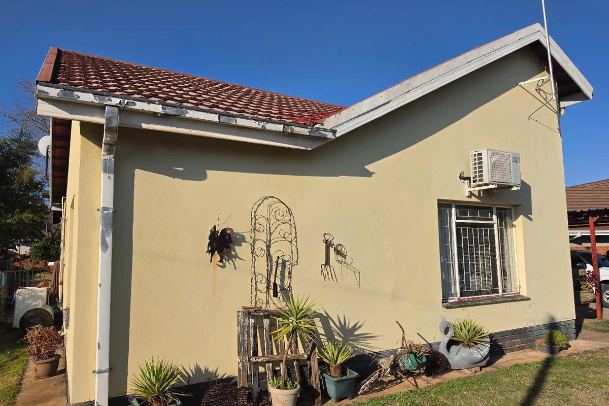 Rear exterior view of the house featuring a tiled roof, wall-mounted air conditioning unit, and security-barred windows with visible maintenance required on fascia and plaster.