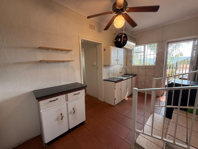 A functional kitchen area featuring tiled flooring, built-in cabinetry, a stainless steel sink, and direct access to an outdoor space via a side door.