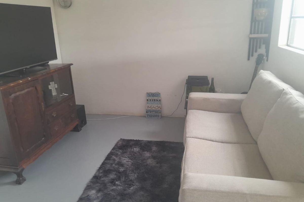 A simple living room area featuring painted concrete flooring and neutral wall finishes, providing a functional space for relaxation.