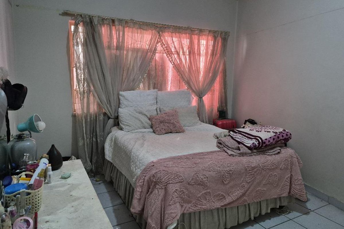 A bedroom featuring tiled flooring and a window with curtain fixtures. The space requires cosmetic updates to improve its overall condition.