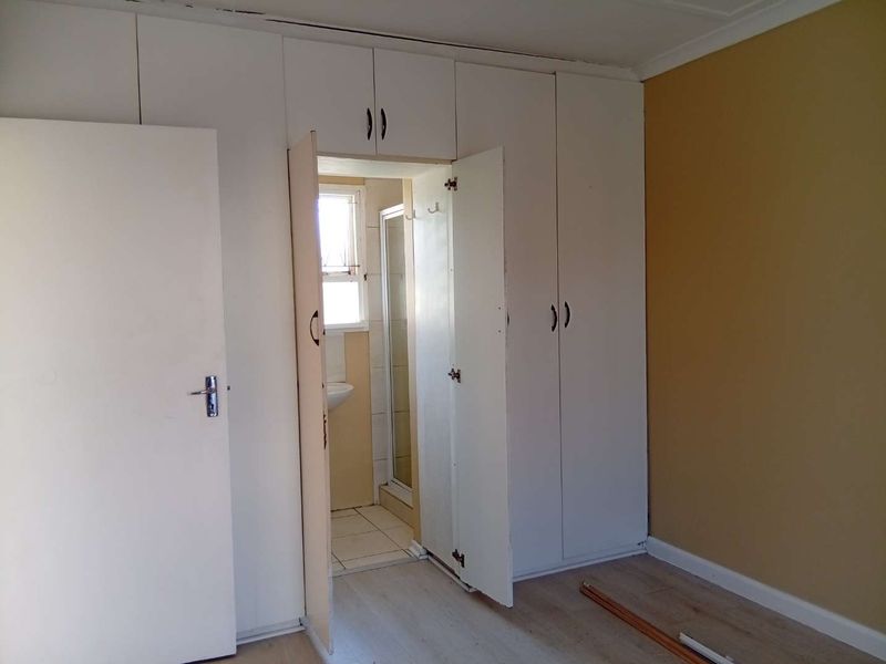 Bedroom featuring built-in cupboards and laminate flooring, with direct access to an en-suite bathroom. The space is vacant and ready for renovation.