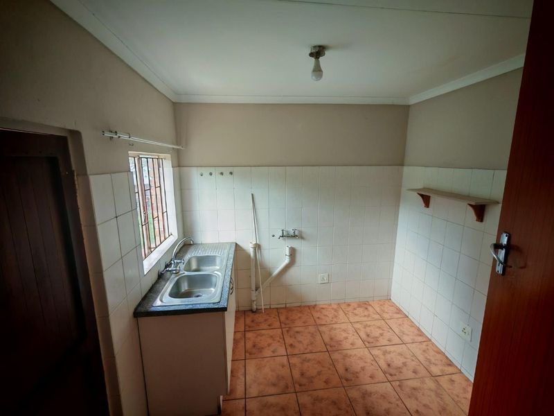 A functional laundry room featuring a double stainless steel sink, tiled splashback, and plumbing connections for appliances, ready for modernization.