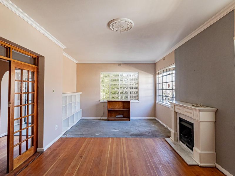 A spacious living room featuring original hardwood floors, a classic fireplace, crown molding, and elegant french doors, offering a blank canvas for renovation.