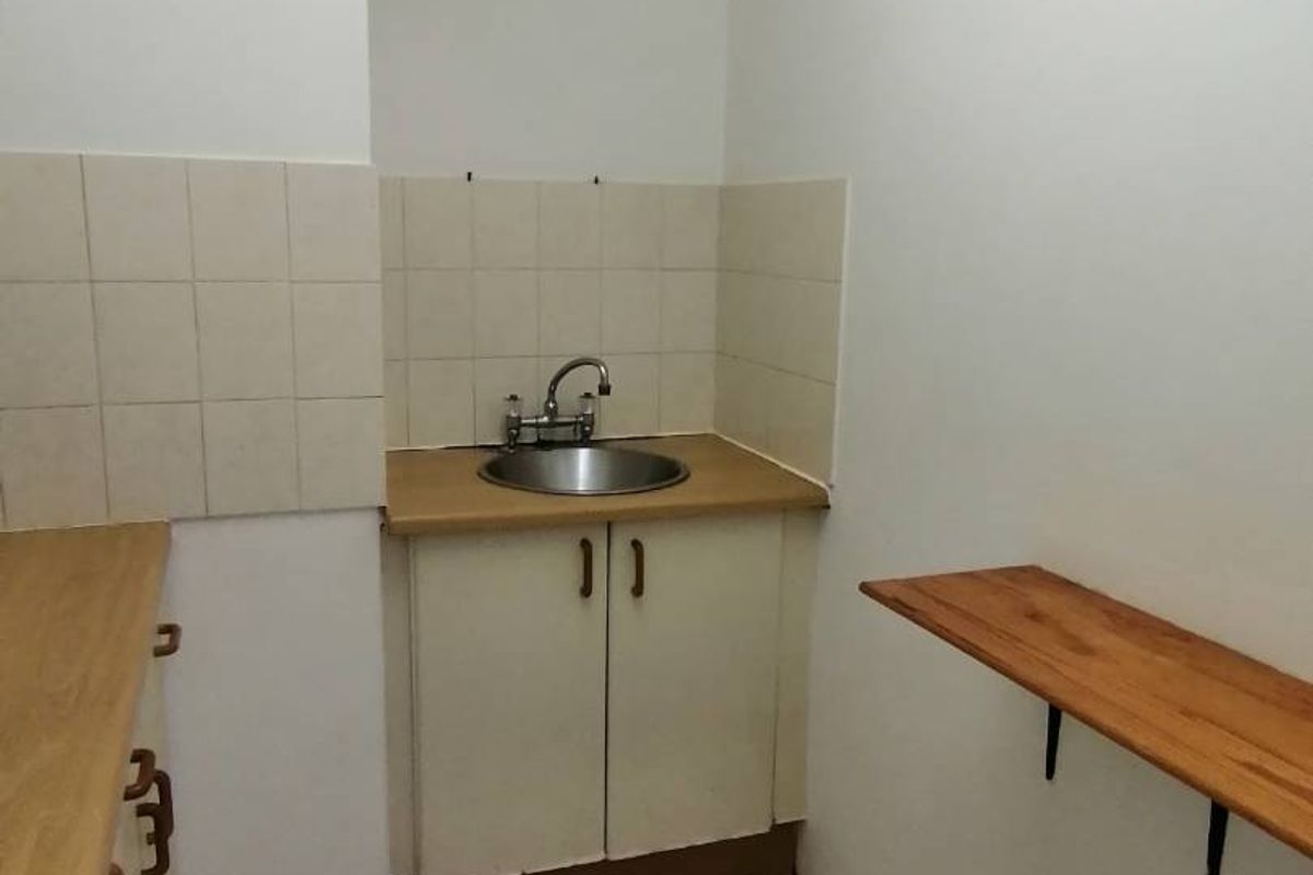 A compact, empty kitchen area featuring a stainless steel sink, tiled splashback, laminate countertops, and basic base cabinetry.