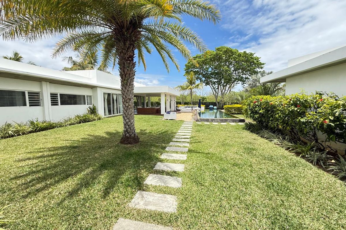 A well-maintained rear garden featuring a manicured lawn, stone paver pathway, and a swimming pool set against the modern exterior of the home.