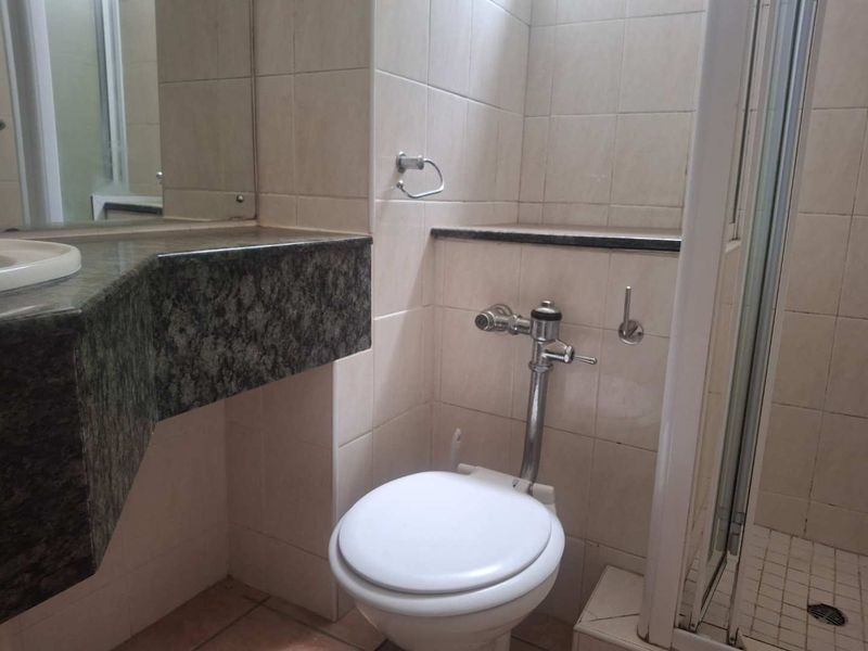 A functional bathroom featuring a flush valve toilet, granite vanity countertop, and a tiled shower enclosure with neutral wall tiling.