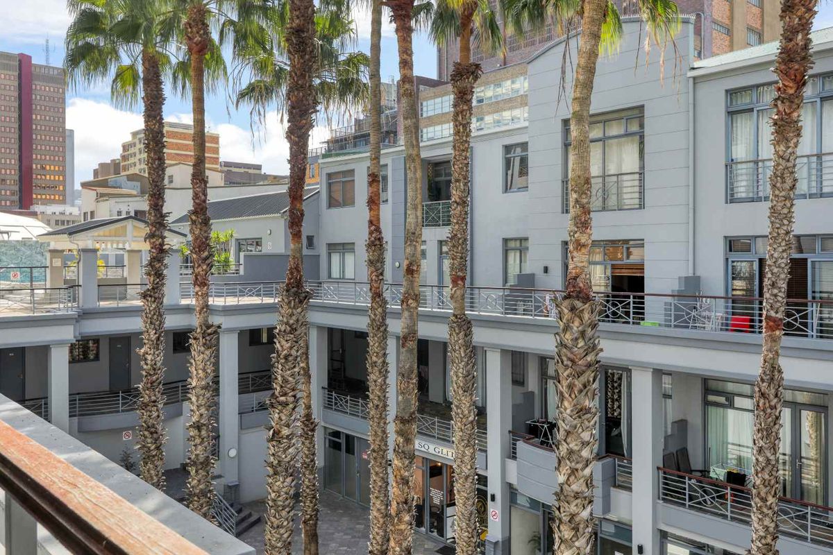 A view of the apartment complex courtyard featuring multiple levels of balconies, metal railings, and established palm trees in a paved central area.