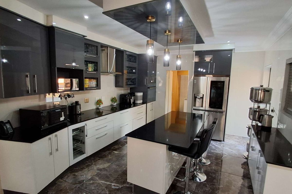 Modern kitchen featuring high-gloss cabinetry, stone countertops, a central island with breakfast bar, and integrated appliances with contemporary lighting.