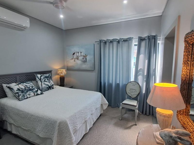 A well-maintained bedroom featuring neutral wall tones, carpeted flooring, a ceiling fan, and a wall-mounted split-system air conditioner.