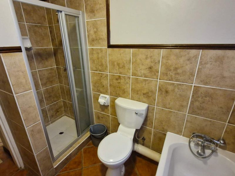A functional bathroom featuring a shower enclosure, bathtub, and toilet with tiled finishes throughout.