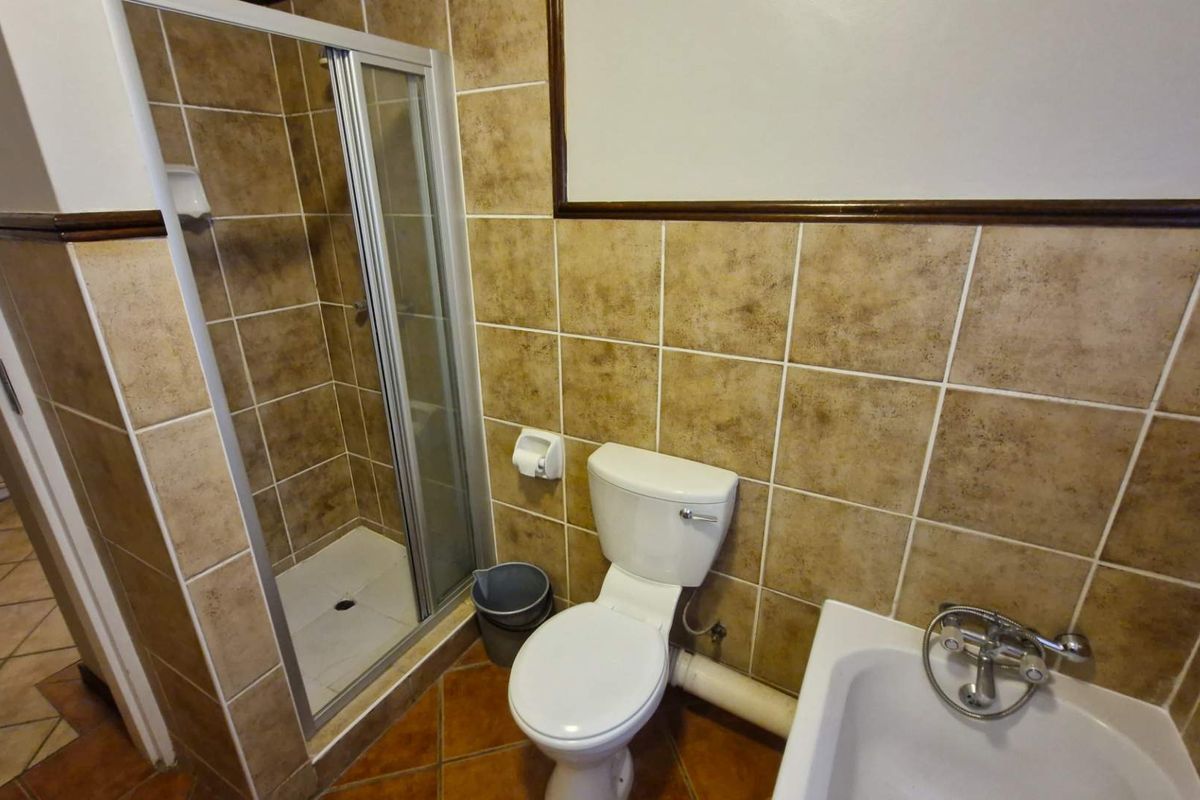 A functional bathroom featuring a shower enclosure, bathtub, and toilet with tiled finishes throughout.