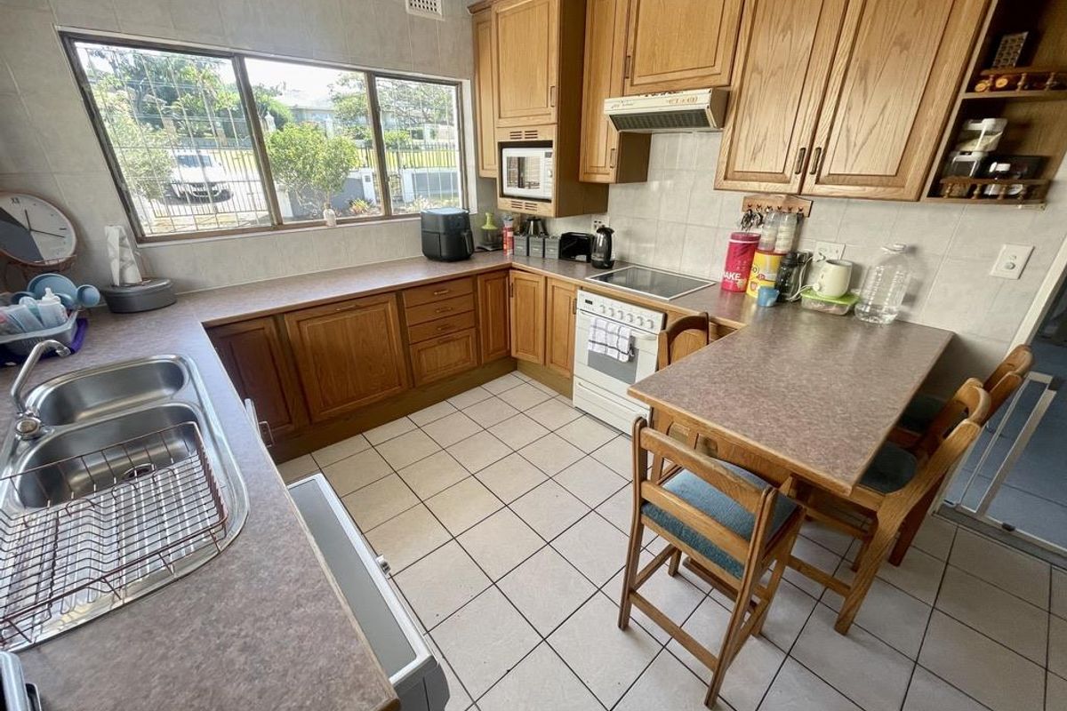 A functional kitchen featuring wooden cabinetry, tiled flooring, a built-in stove with extractor fan, and a breakfast nook area.