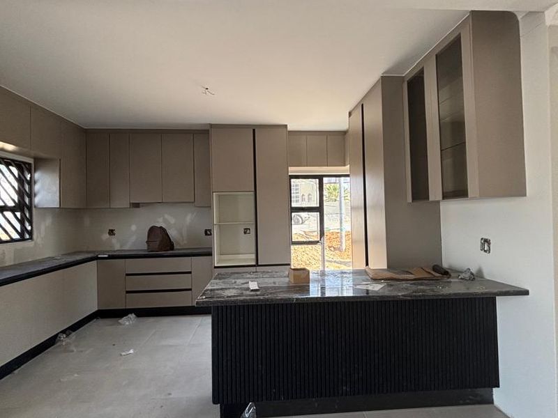 Modern kitchen featuring neutral cabinetry, a stone-topped island with fluted detailing, and large format floor tiles, currently in the final stages of completion.