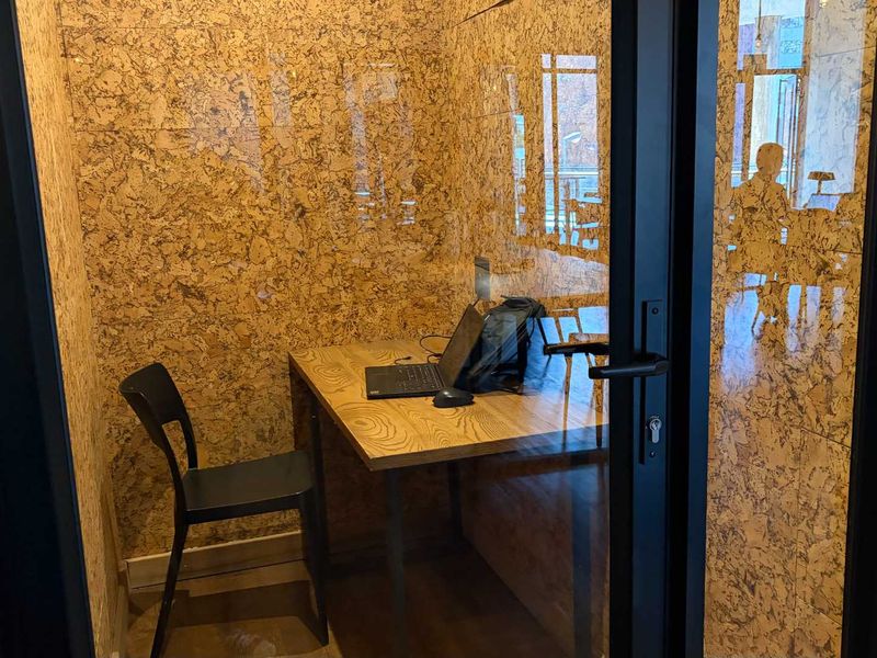 A compact, private office pod featuring sound-dampening cork wall paneling and a modern glass-paneled door, ideal for focused work.