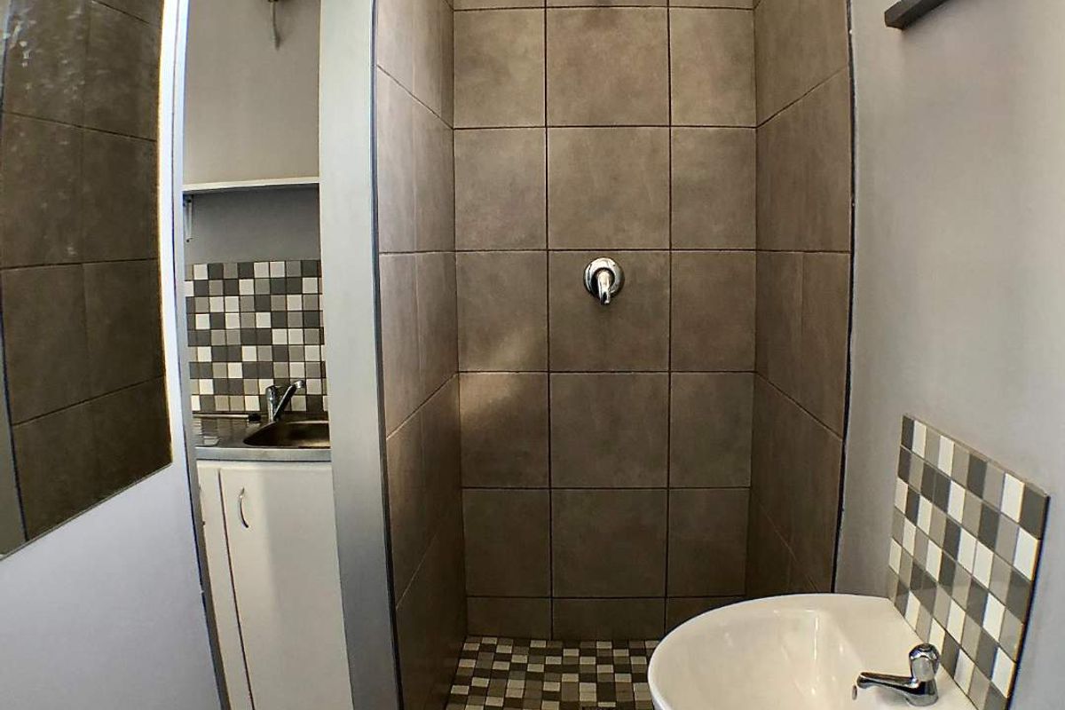 Compact bathroom featuring a tiled walk-in shower with modern fixtures and a wall-mounted basin with a decorative mosaic tile splashback.