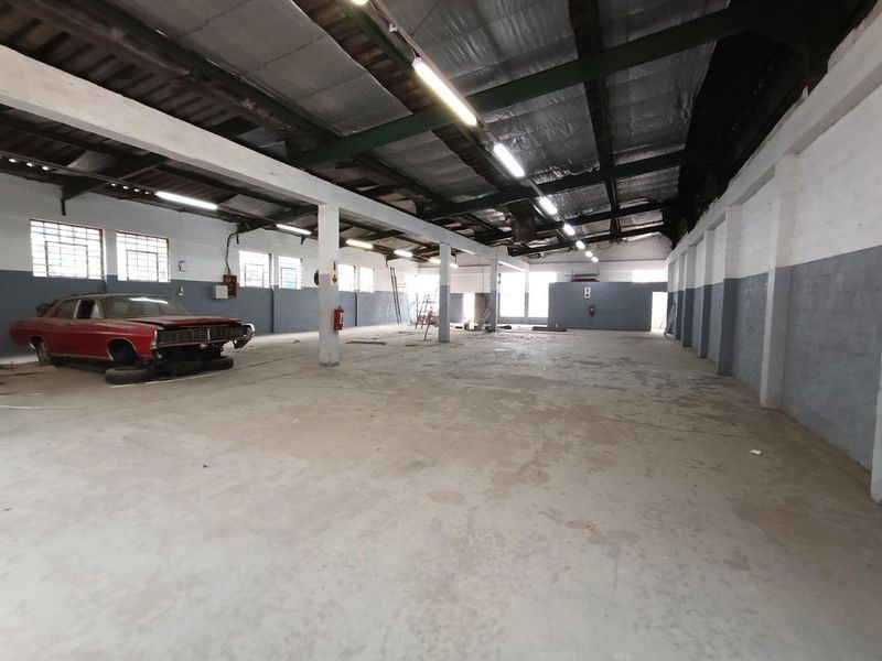 Spacious industrial warehouse unit featuring high ceilings with exposed steel trusses, concrete flooring, and ample natural light through steel-framed windows.
