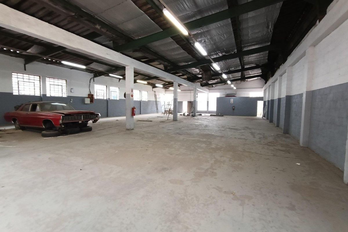 Spacious industrial warehouse unit featuring high ceilings with exposed steel trusses, concrete flooring, and ample natural light through steel-framed windows.