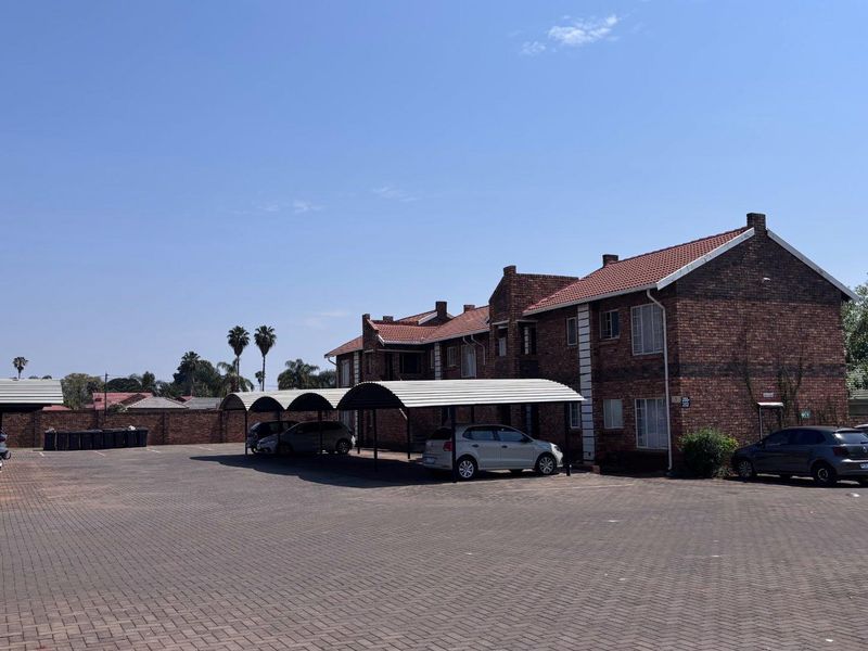 Exterior view of a brick apartment complex featuring a large paved parking area with multiple covered carport bays.