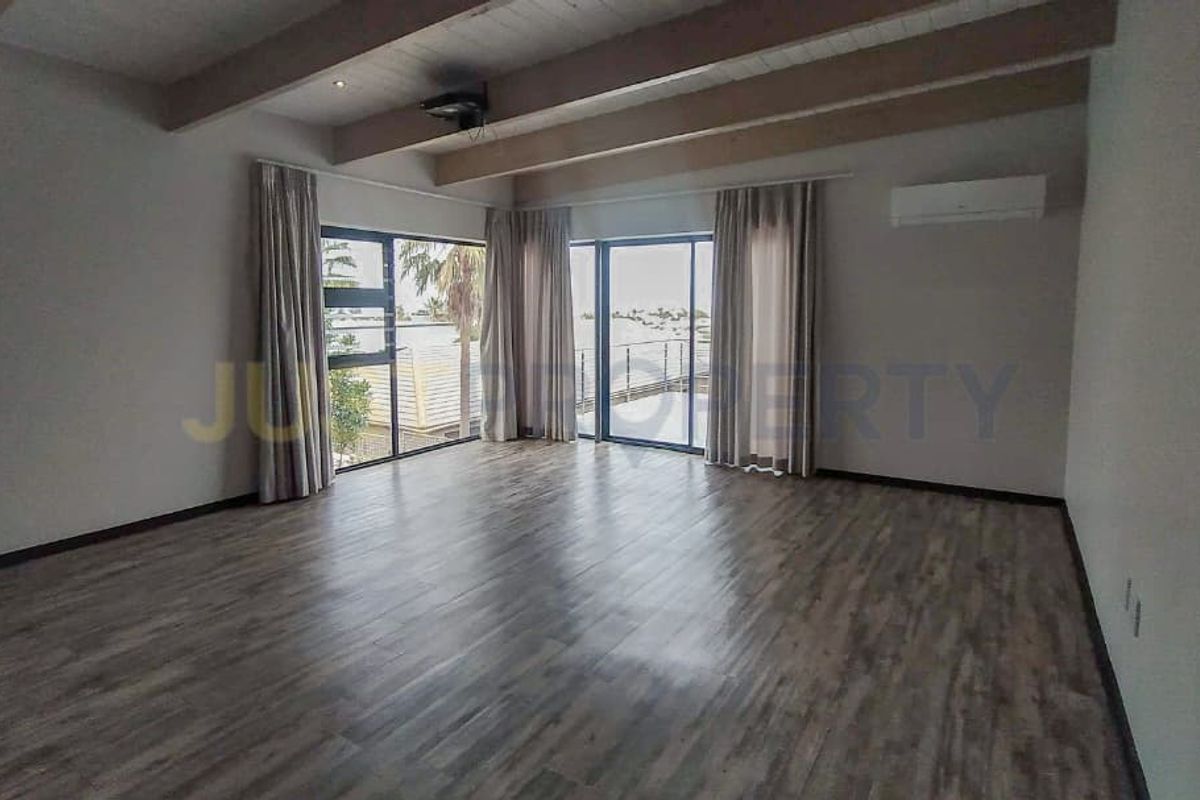 Spacious living area featuring exposed timber ceiling beams, wood-look flooring, and large sliding glass doors providing access to an outdoor balcony.
