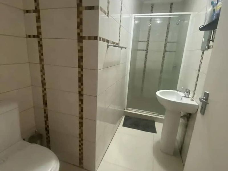 A functional bathroom featuring a pedestal basin, toilet, and a glass-enclosed shower with tiled walls and flooring.