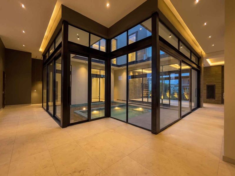 A modern indoor swimming pool area featuring floor-to-ceiling glass walls, recessed lighting, and high-quality tiled flooring, creating a seamless transition between indoor spaces.