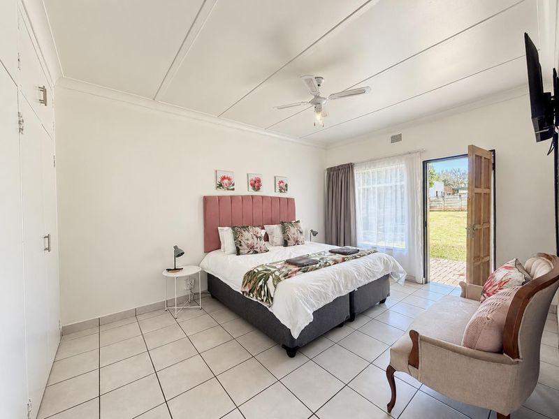 A bright bedroom featuring tiled flooring, built-in cupboards, a ceiling fan, and direct access to the rear garden through a sliding door.