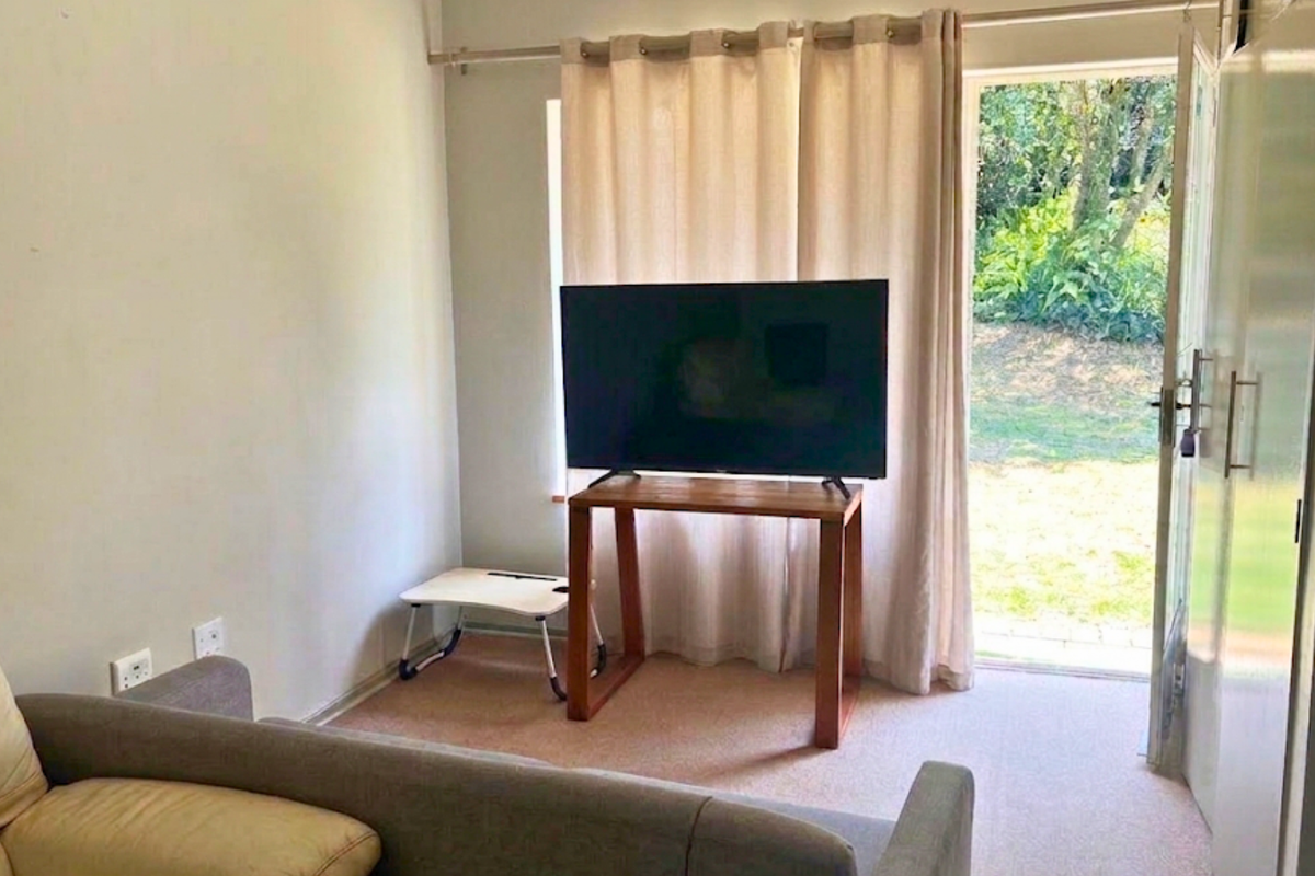 A living room area featuring neutral walls, carpeted flooring, and direct access to an outdoor garden space through a glass door.
