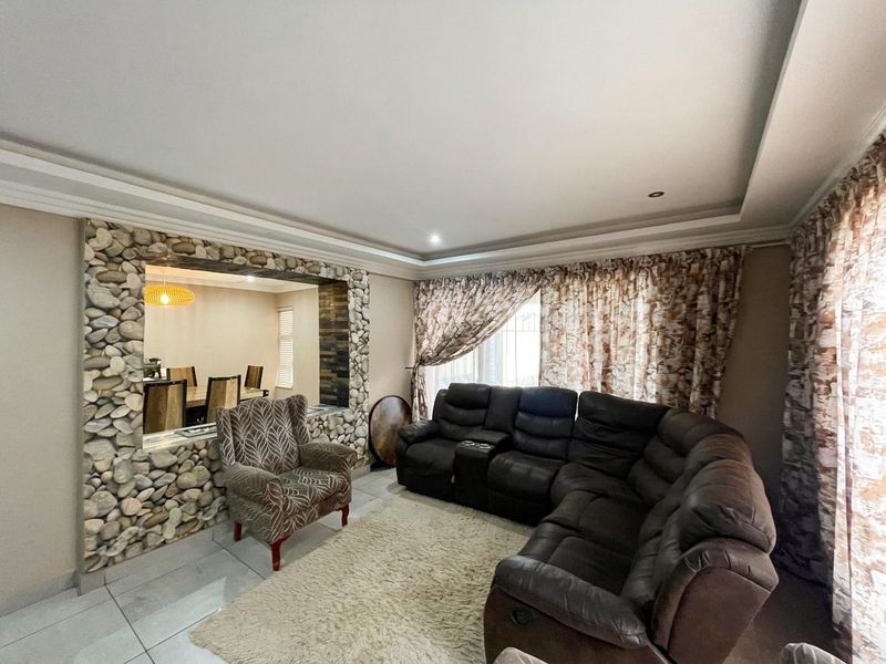 Spacious living room featuring a decorative stone accent wall, recessed ceiling detail, and neutral tiled flooring, offering a comfortable and distinct living space.