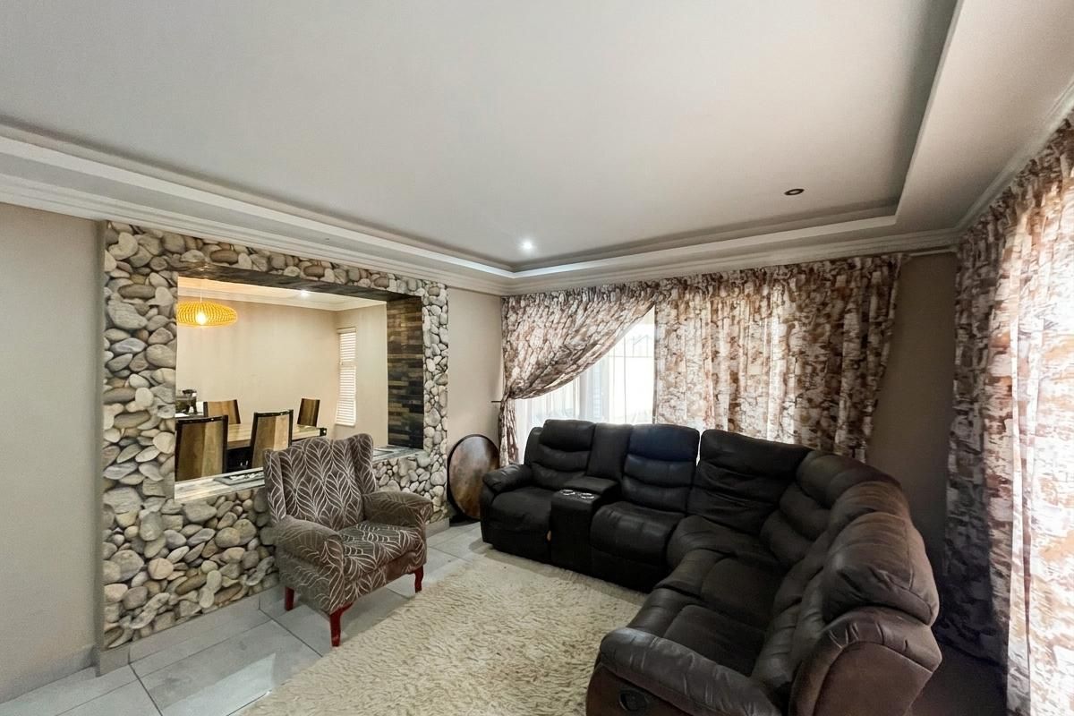 Spacious living room featuring a decorative stone accent wall, recessed ceiling detail, and neutral tiled flooring, offering a comfortable and distinct living space.