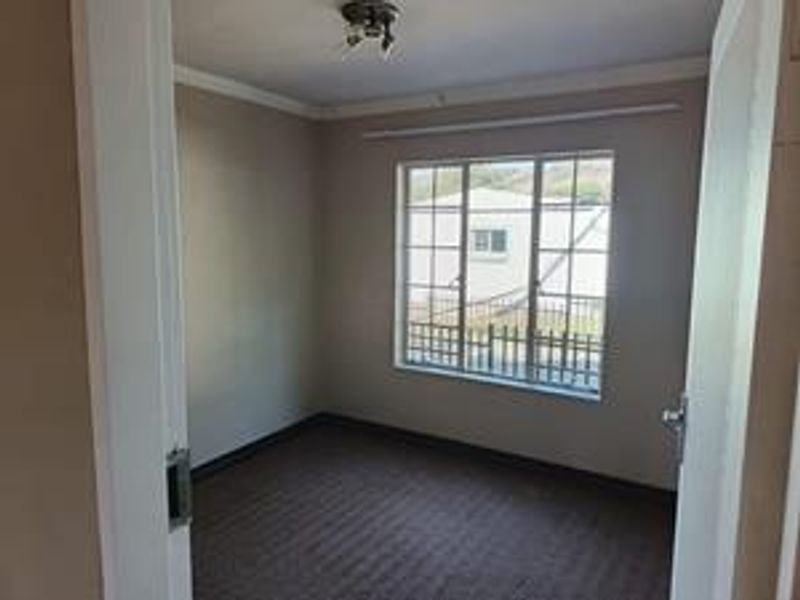 An empty bedroom featuring carpeted flooring, a window with security bars, and a central ceiling light fixture.