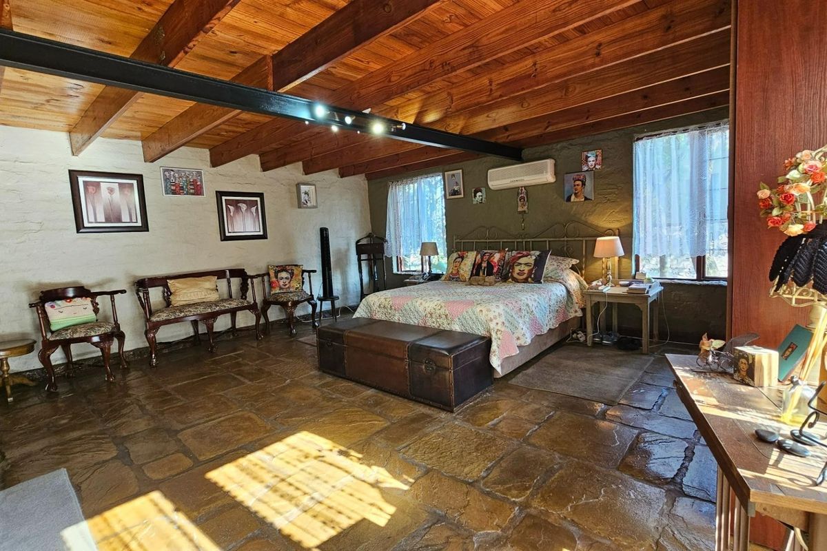 Spacious bedroom featuring exposed timber beam ceilings, rustic stone flooring, and textured walls, creating a warm and character-filled living space.