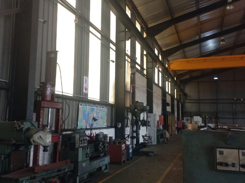 Spacious industrial workshop featuring high ceilings, overhead crane infrastructure, and large windows providing natural light for manufacturing or storage operations.