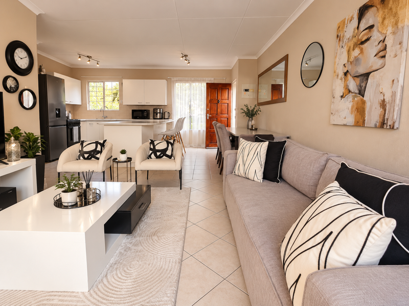 A bright open-plan living and kitchen area featuring tiled flooring, modern cabinetry, a central kitchen island, and direct access to the main entrance.