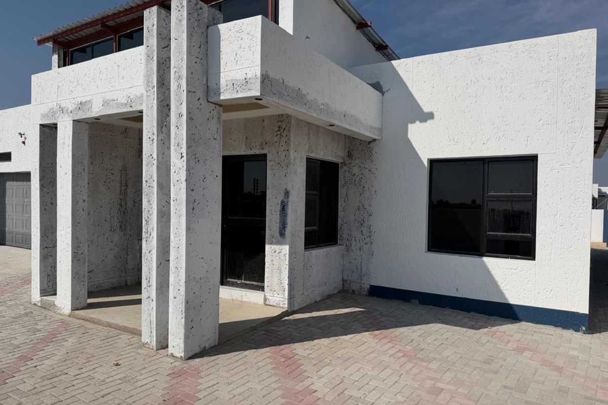 Front elevation of a house featuring a paved driveway, covered entrance, and unfinished exterior wall finishes.